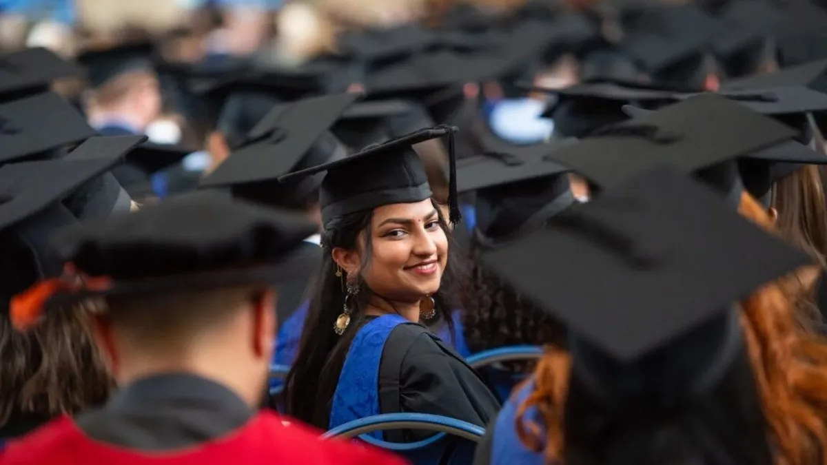 An Indian graduate smiling in a black graduation cap and gown at a UK university ceremony