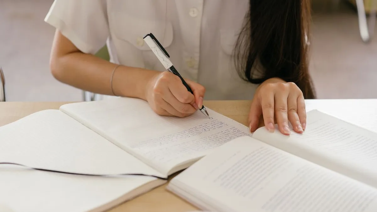A student handwriting notes in a notebook while studying