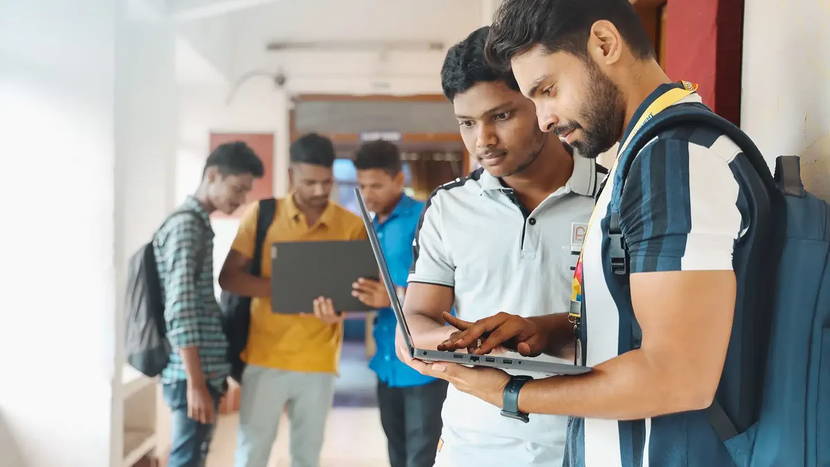 Indian college students looking at a laptop in a college corridor