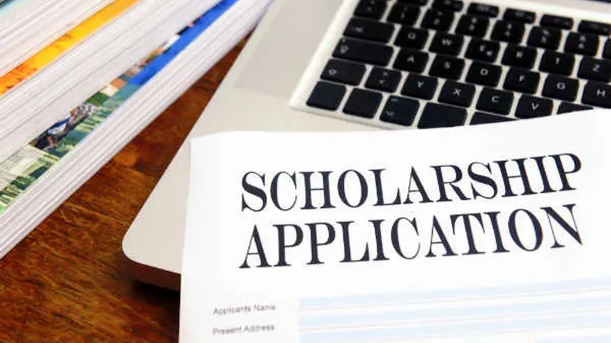 A printed scholarship application form lying next to a laptop on a student's desk